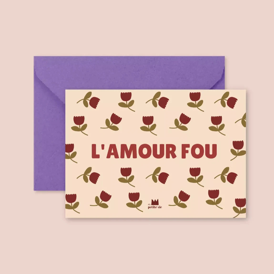 A greeting postcard with a cream background, featuring a repeating pattern of small red flowers with olive-green leaves. Bold red text in the centre reads "L'AMOUR FOU". The card is paired with a deep purple envelope.