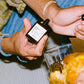 Person holding a glass with a drink and a small bottle, with food on a plate in the foreground.