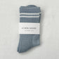 A pair of ribbed grey socks featuring red and blue stripes at the cuffs and "Le Bon Shoppe" branding on the foot, laid flat on a textured surface.