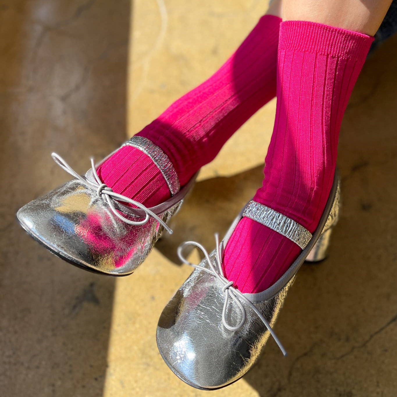 A pair of vibrant fuchsia ribbed socks, styled with silver ballet flats and showcased in soft natural lighting.