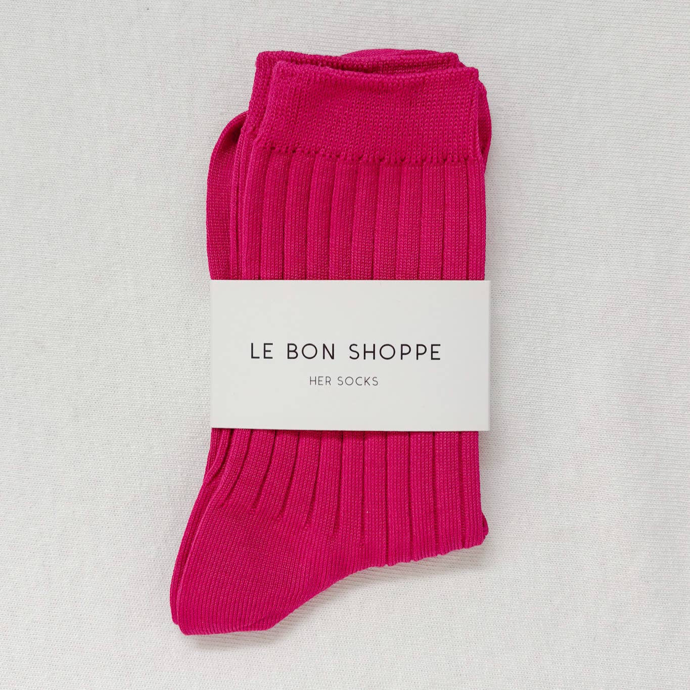 A pair of neatly folded fuchsia ribbed crew socks wrapped with a "Le Bon Shoppe Her Socks" label.