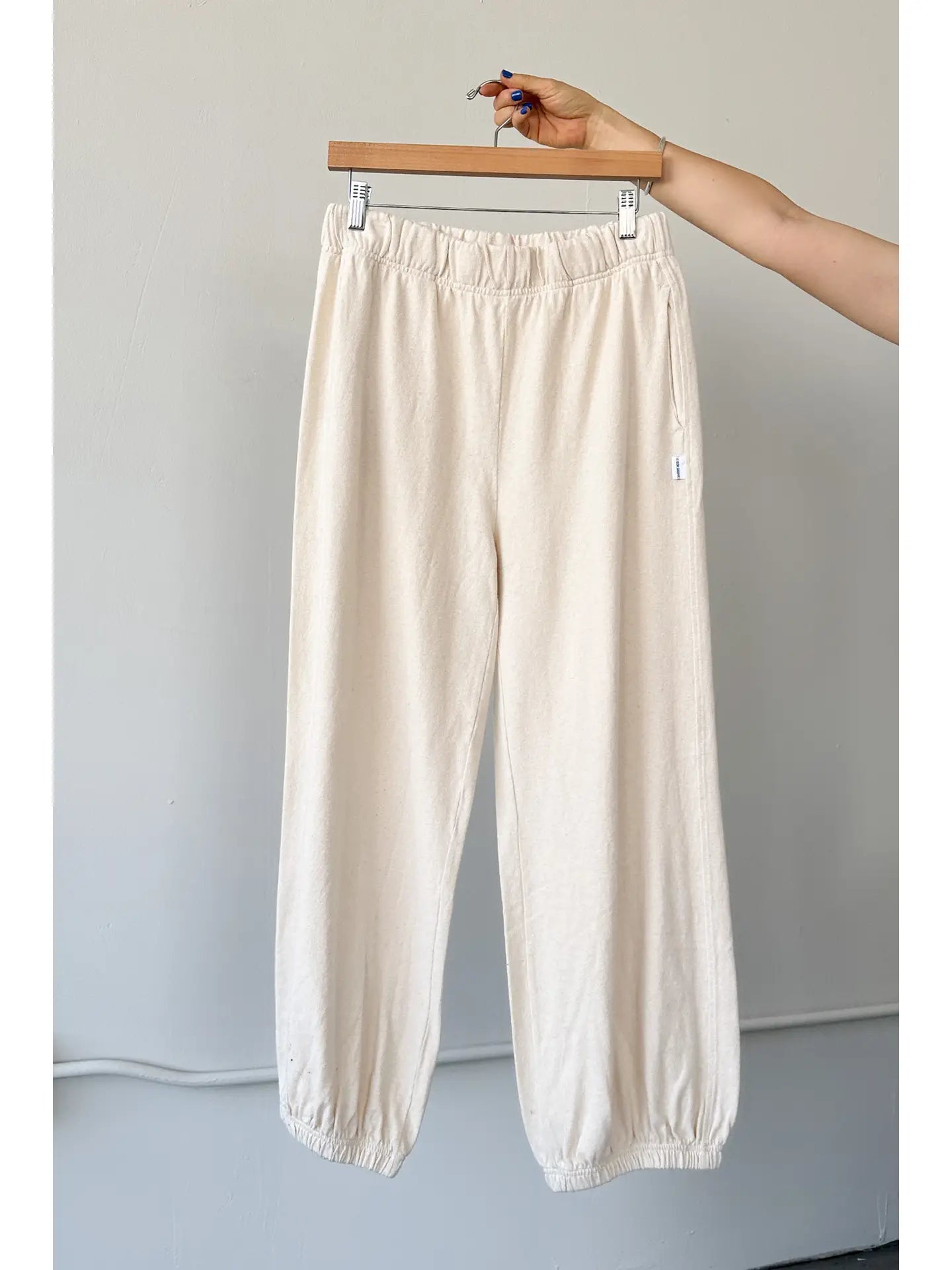 Balloon Pants in Natural hanging on a wooden hanger – Displayed against a minimal backdrop, highlighting the relaxed fit, deep pockets, and gathered ankle details.