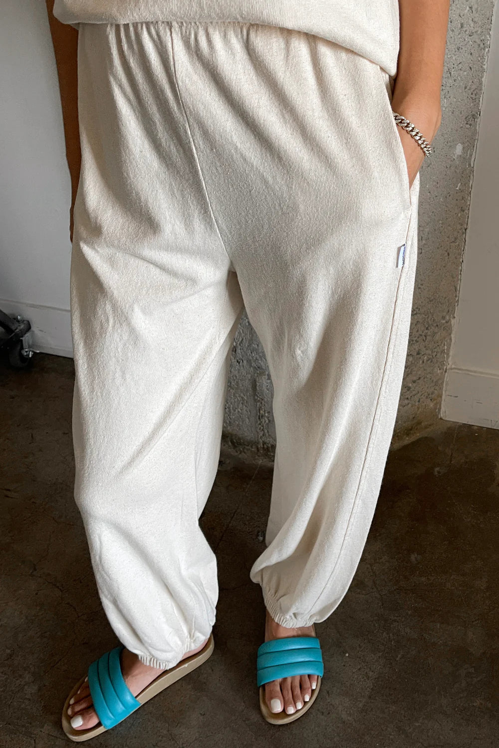 A close-up of the Natural Balloon Pants, showcasing their soft, textured fabric, elastic waistband, and relaxed fit. Styled with bright blue sandals for a casual look.