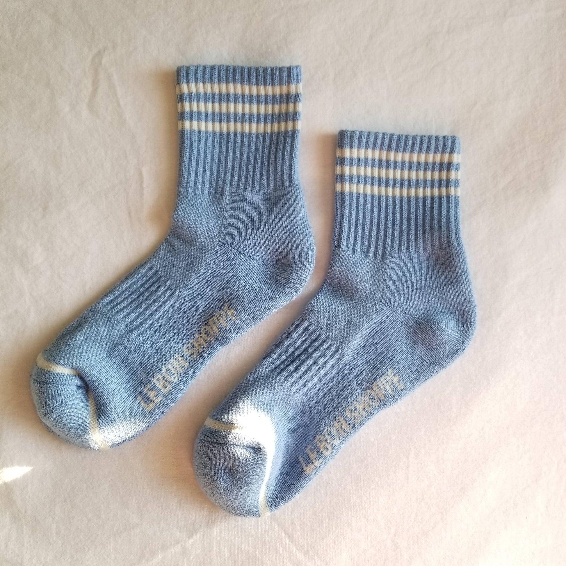 A pair of blue crew-length socks with a triple-contrast stripe at the top, branded with 'Le Bon Shoppe'.