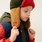 The model with short blonde hair wears the Liewood Bravo Pile Hat in Army Brown/Multi Mix, featuring brown, navy blue, and red color tones, with soft fleece lining, earflaps, and adjustable snap-button straps. He wears a matching padded jacket