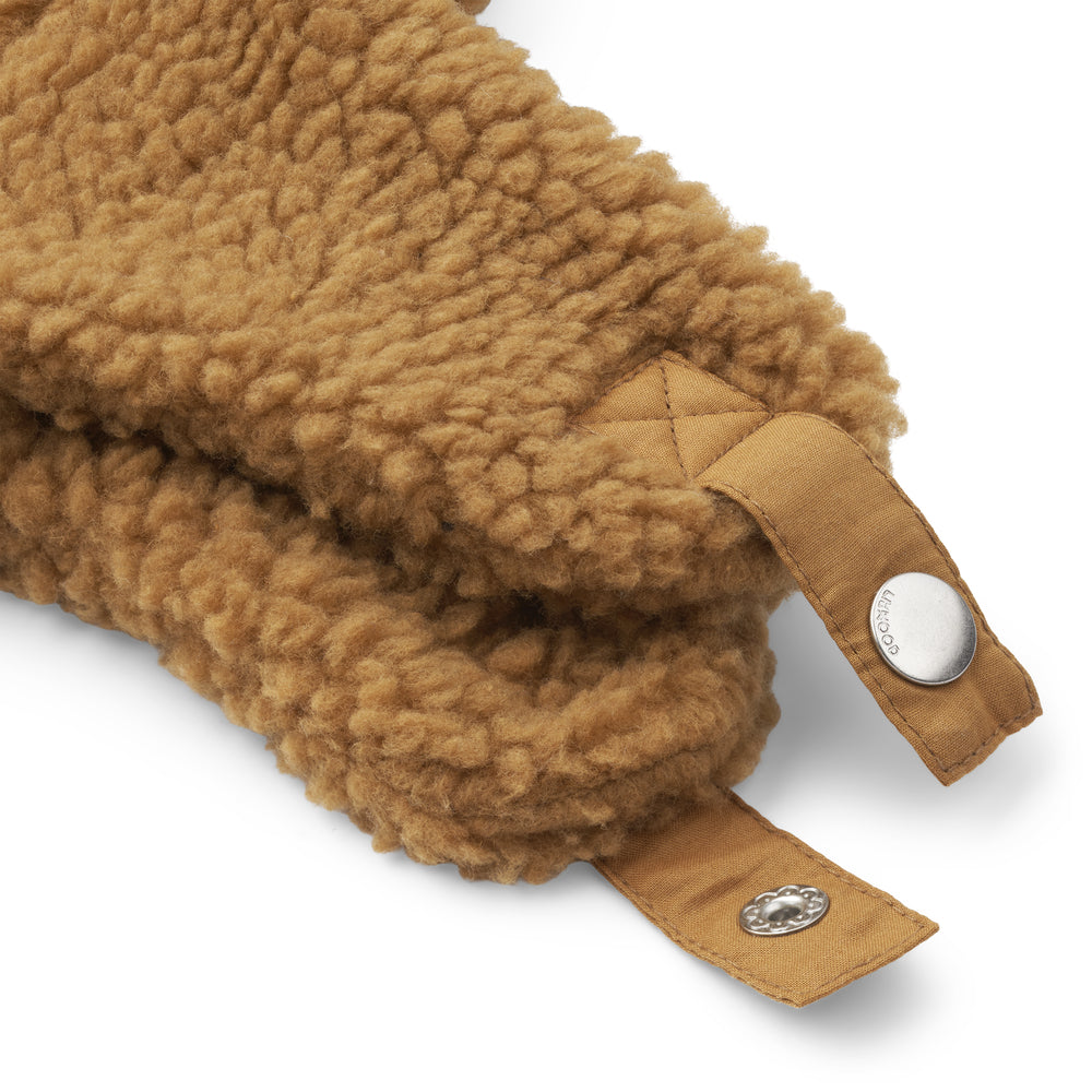 A close up of the chin strap of the Liewood Golden Caramel Bravo Pile Hat for children, featuring soft fleece lining, protective earflaps, and adjustable snap-button straps. 