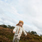 Liewood Golden Caramel Bravo Pile Hat for children, featuring soft fleece lining, protective earflaps, and adjustable snap-button straps. The model runs outside in a cream  fleece jacket and beige cords