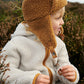 Liewood Golden Caramel Bravo Pile Hat for children, featuring soft fleece lining, protective earflaps, and adjustable snap-button straps. The model looks to the side in a cream  fleece jacket and beige cords