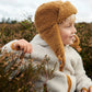 Liewood Golden Caramel Bravo Pile Hat for children, featuring soft fleece lining, protective earflaps, and adjustable snap-button straps. The model looks to the side in a cream  fleece jacket