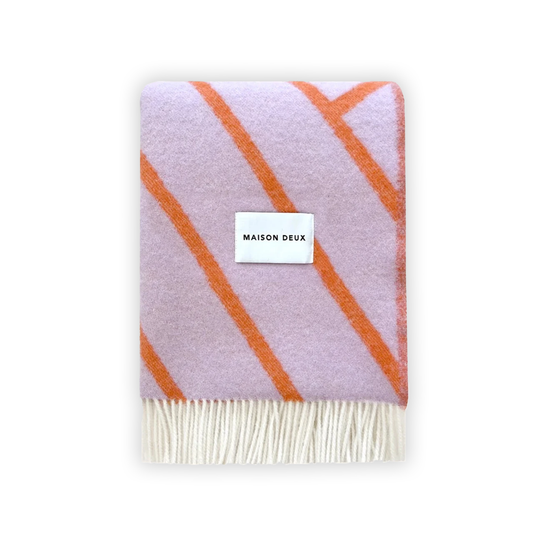 A folded Maison Deux blanket with lilac and orange lines and fringes on the short sides, displaying the brand name on a white label.