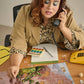 Woman multitasking at a desk, talking on the phone and working on a puzzle.