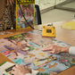 Person working on a puzzle with a box of puzzles and a yellow phone in the background.