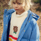 Child wearing a blue puffer jacket over a sweater with a bear design outdoors.