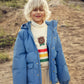 Child wearing a blue puffer jacket and a sweater with a bear design outdoors.