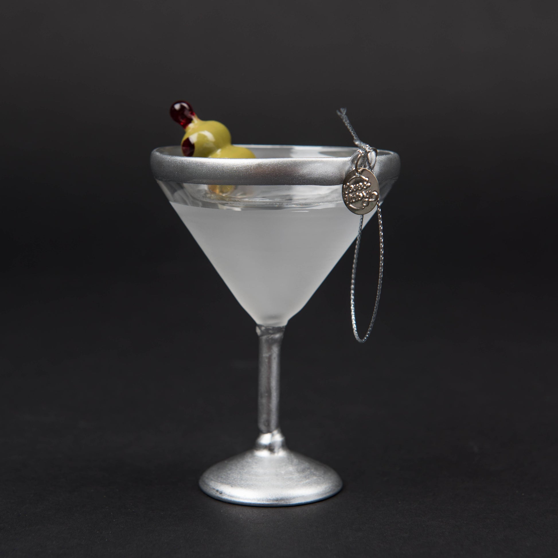 Hand-blown glass Martini ornament featuring a classic stemmed martini glass with a hand-painted olive garnish, measuring 4.5" x 3". Comes with a glittery silver hanging loop and a round L&V charm