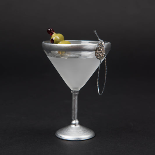 Hand-blown glass Martini ornament featuring a classic stemmed martini glass with a hand-painted olive garnish, measuring 4.5" x 3". Comes with a glittery silver hanging loop and a round L&V charm