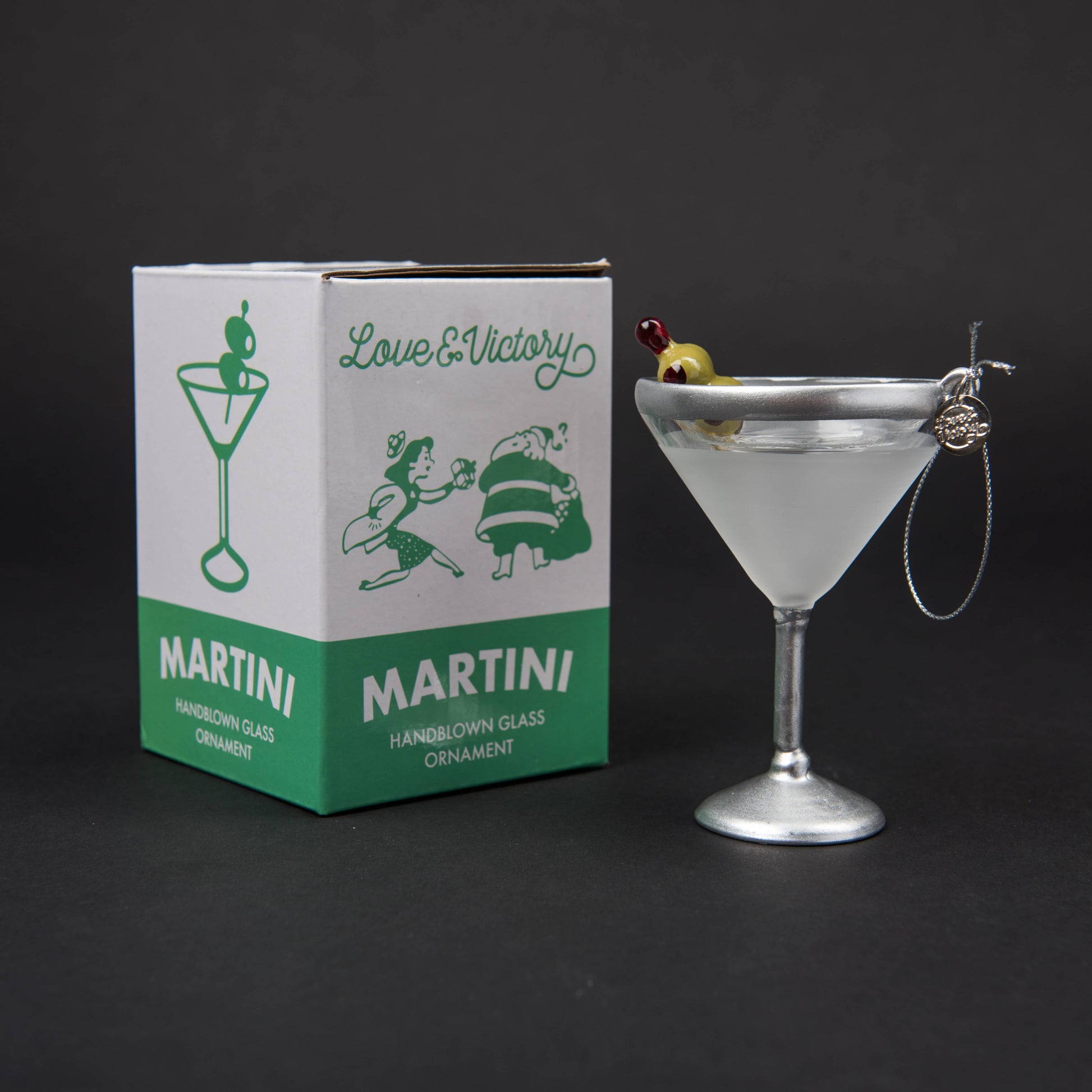 Hand-blown glass Martini ornament featuring a classic stemmed martini glass with a hand-painted olive garnish, measuring 4.5" x 3". Comes with a glittery silver hanging loop and a round L&V charm, packaged in a custom retro holiday box.