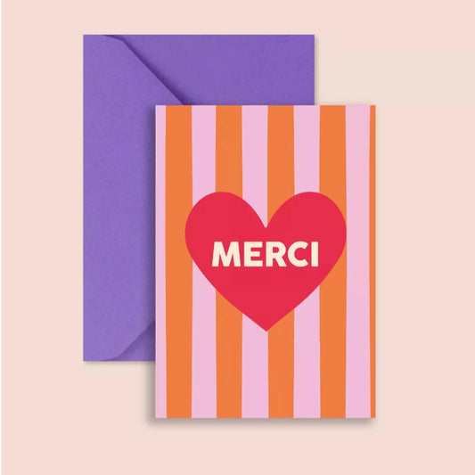 A postcard with a bold pink and orange striped background. A large red heart sits in the centre with the word "MERCI" in white capital letters. The card is paired with a deep purple envelope.