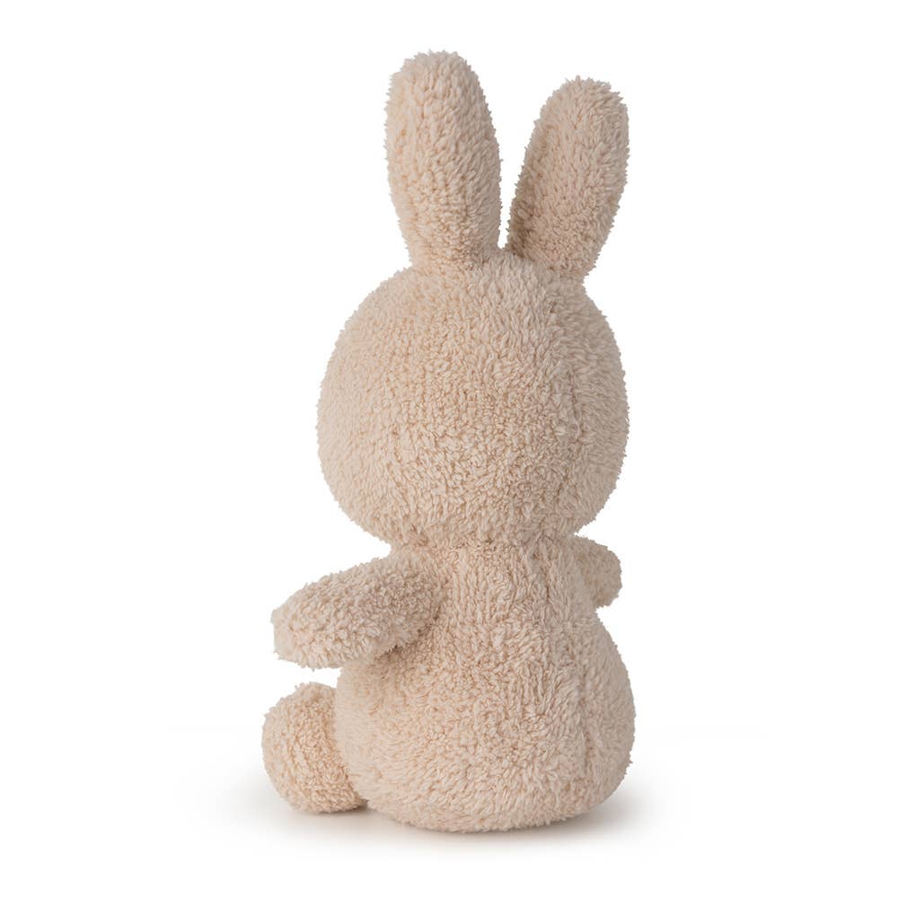 A MiffyTerry soft toy in the colour beige. This Miffy has black eyes and mouth. Miffy is 23 cm in height. The background is white. This is the back side of Miffy. 