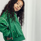 A side-angle portrait of a child wearing the Mini Rodini Note Chenille Satin Baseball Jacket, showing off its glossy satin fabric, relaxed silhouette, and structured collar.