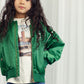 Mid-shot of child wearing jacket: A closer look at the Mini Rodini Note Chenille Satin Baseball Jacket worn over a printed t-shirt, with gold zipper details and embroidered accents visible.