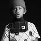 Black and white photo of a child wearing a patterned shirt and knitted hat.