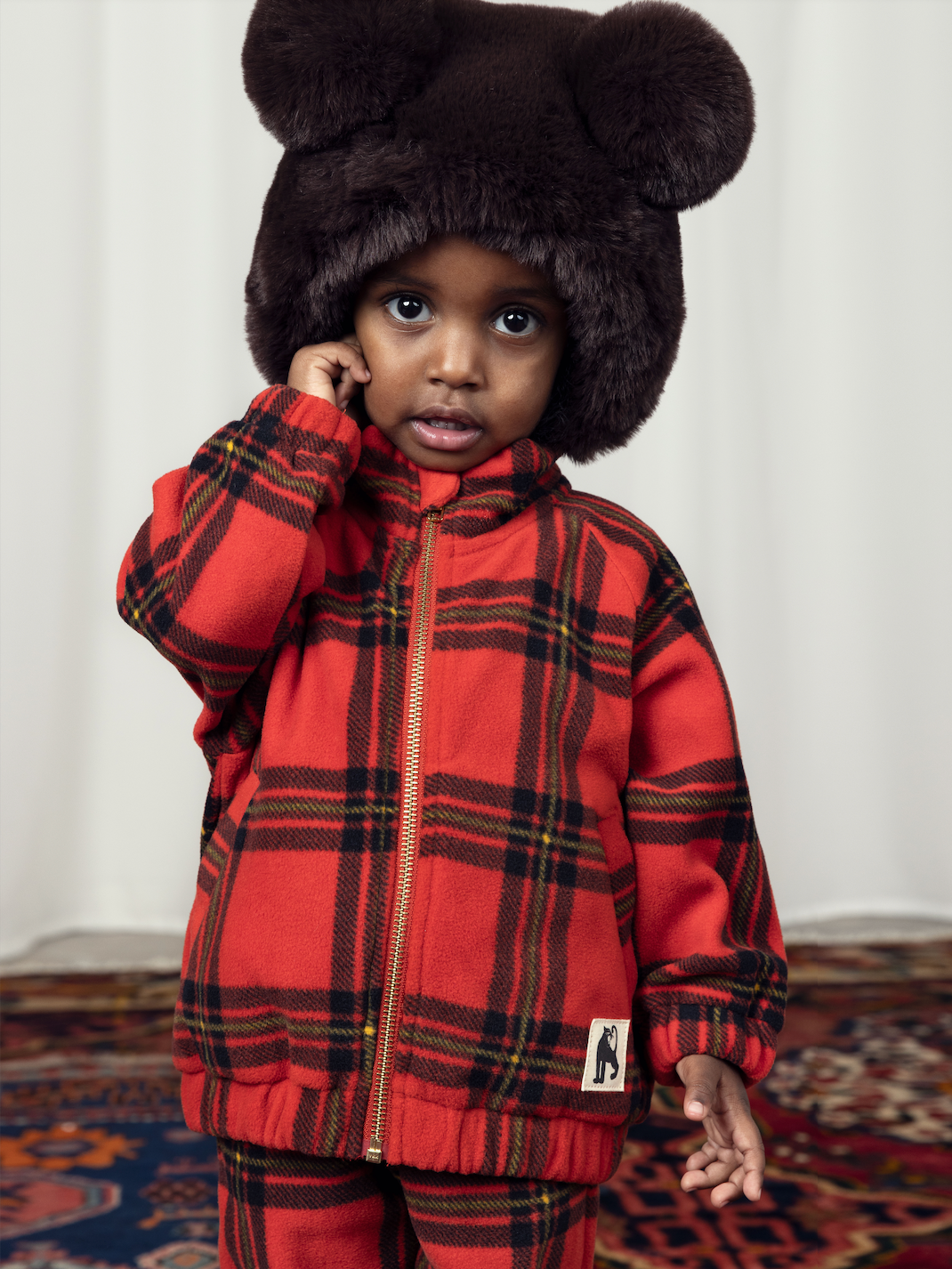 a child in the Mini Rodini children bright red with large check pattern fleece jacket, with a gold plated zip and two side pockets and a high neck