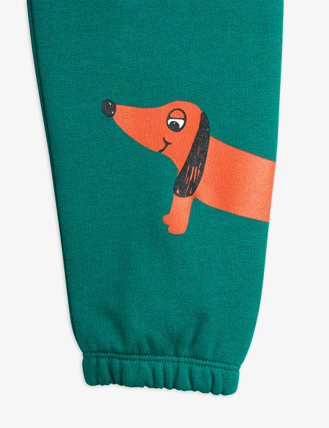 a pair of teal green mini rodini sweatpants with a printed red sausage dog on the bottom of the left leg. with an elasticated waistband and cuffs at the ankles