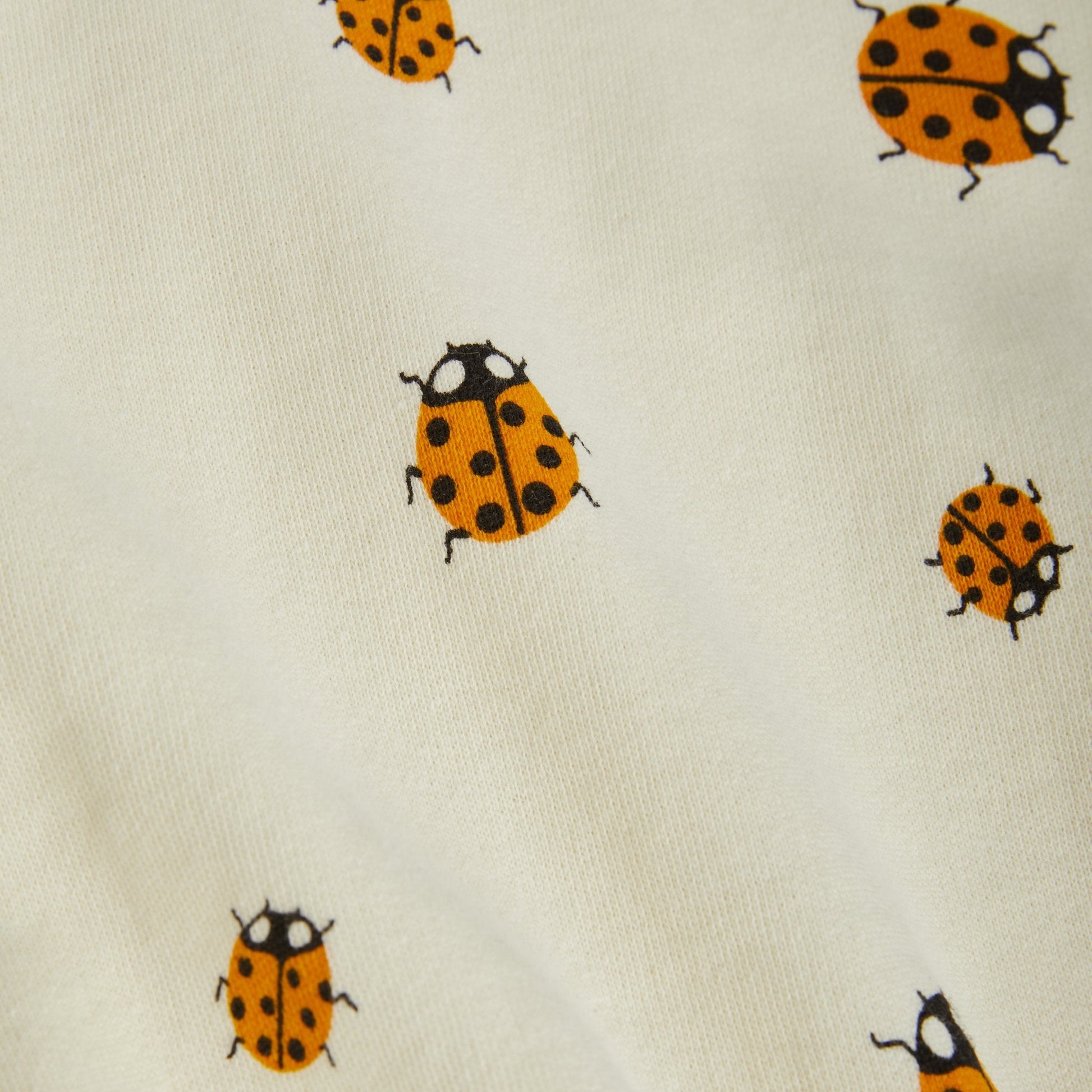  A detailed view of the soft organic cotton material, highlighting the vibrant orange and black ladybird print against the off-white base.