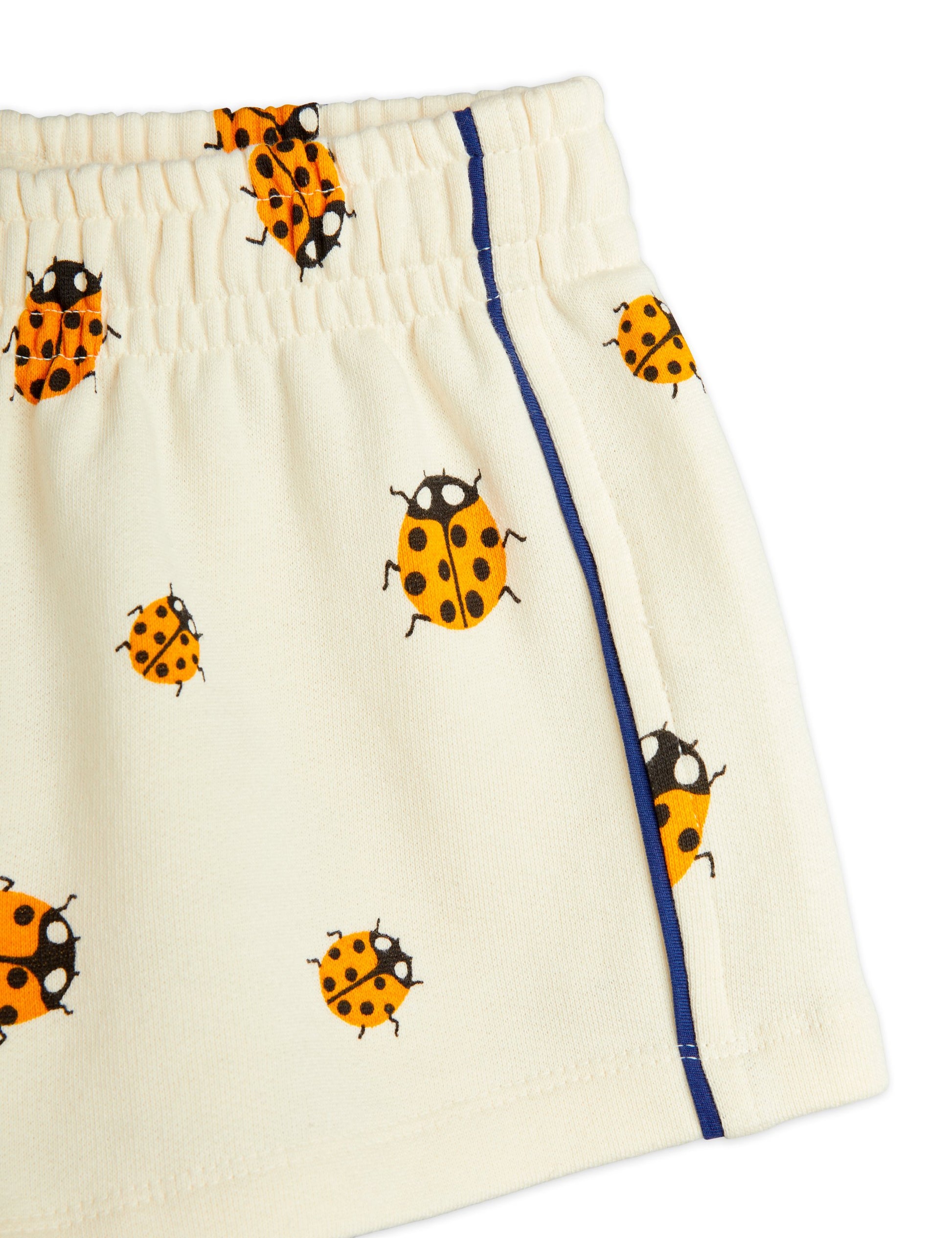 A detailed close-up of the shorts' elasticated waistband, navy blue side piping, and ladybird print on soft, breathable fabric.