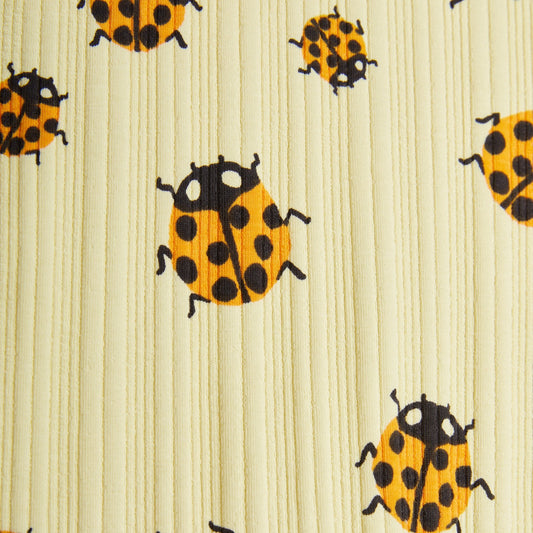 A detailed close-up of the ribbed texture and playful orange and black ladybird print on soft yellow organic cotton fabric.