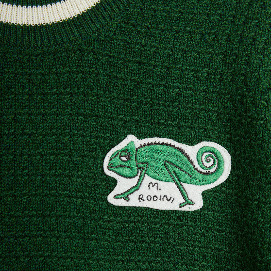Close-up of the embroidered chameleon patch on the Mini Rodini green knit tee.