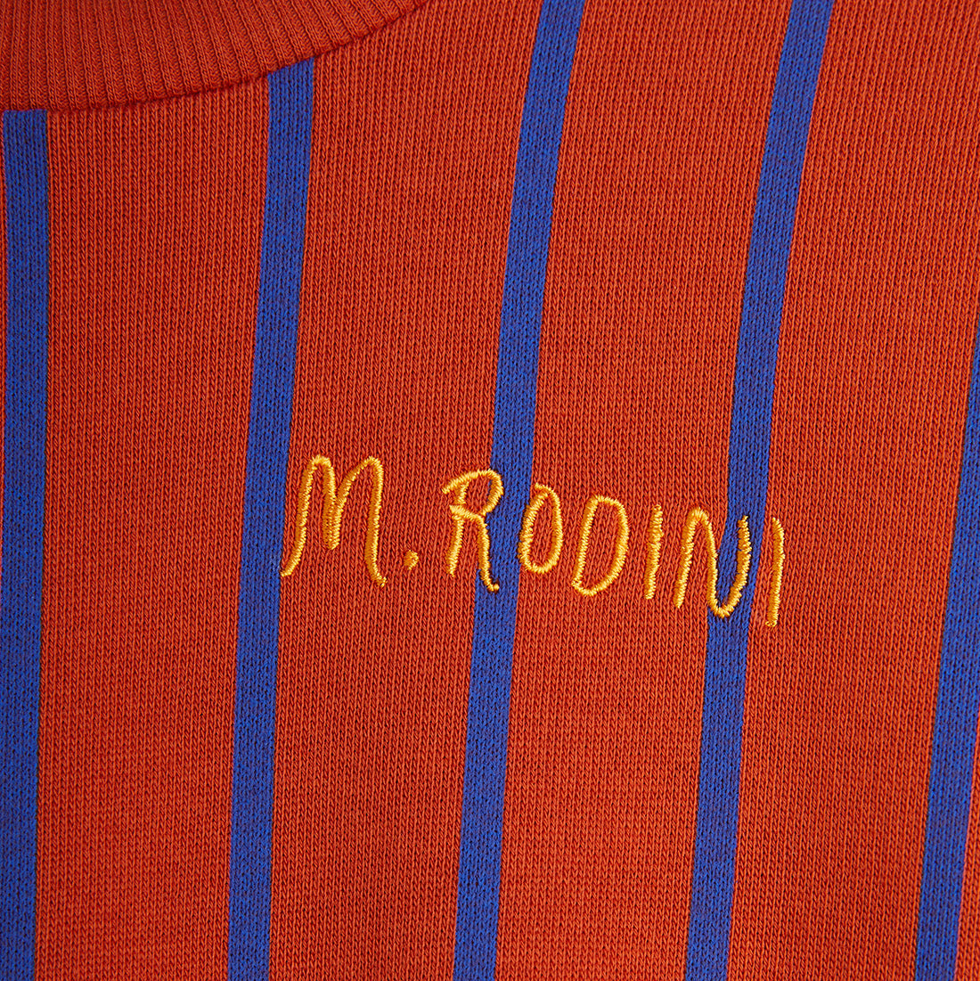 Close-up of the embroidered "M. Rodini" logo in yellow on the chest of the red Mini Rodini stripe sweatshirt.