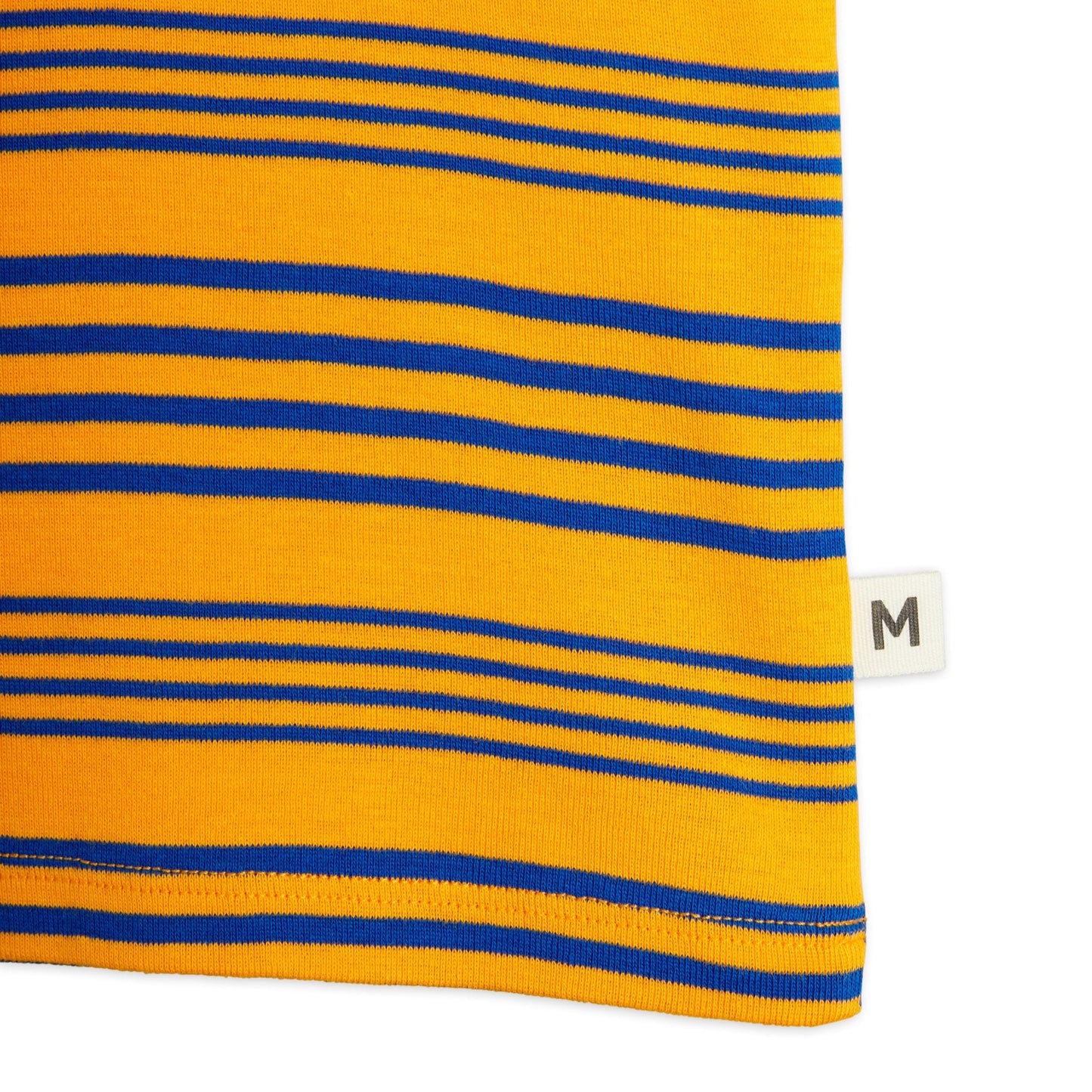 A detailed view of the hem of the Mini Rodini Stripe Tank, showing the fine ribbed trim, horizontal blue stripes on a yellow background, and a small "M" brand label stitched on the side.