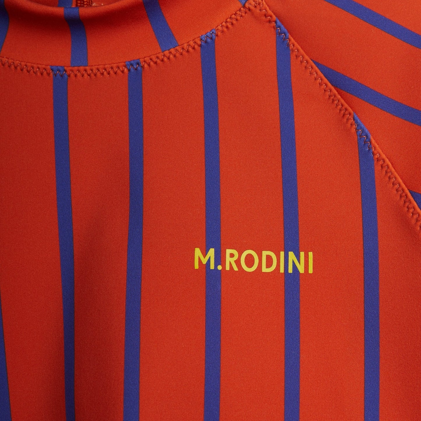  A detailed close-up of the "M. Rodini" logo, showcasing the bold striped design and smooth, stretchy swim fabric.