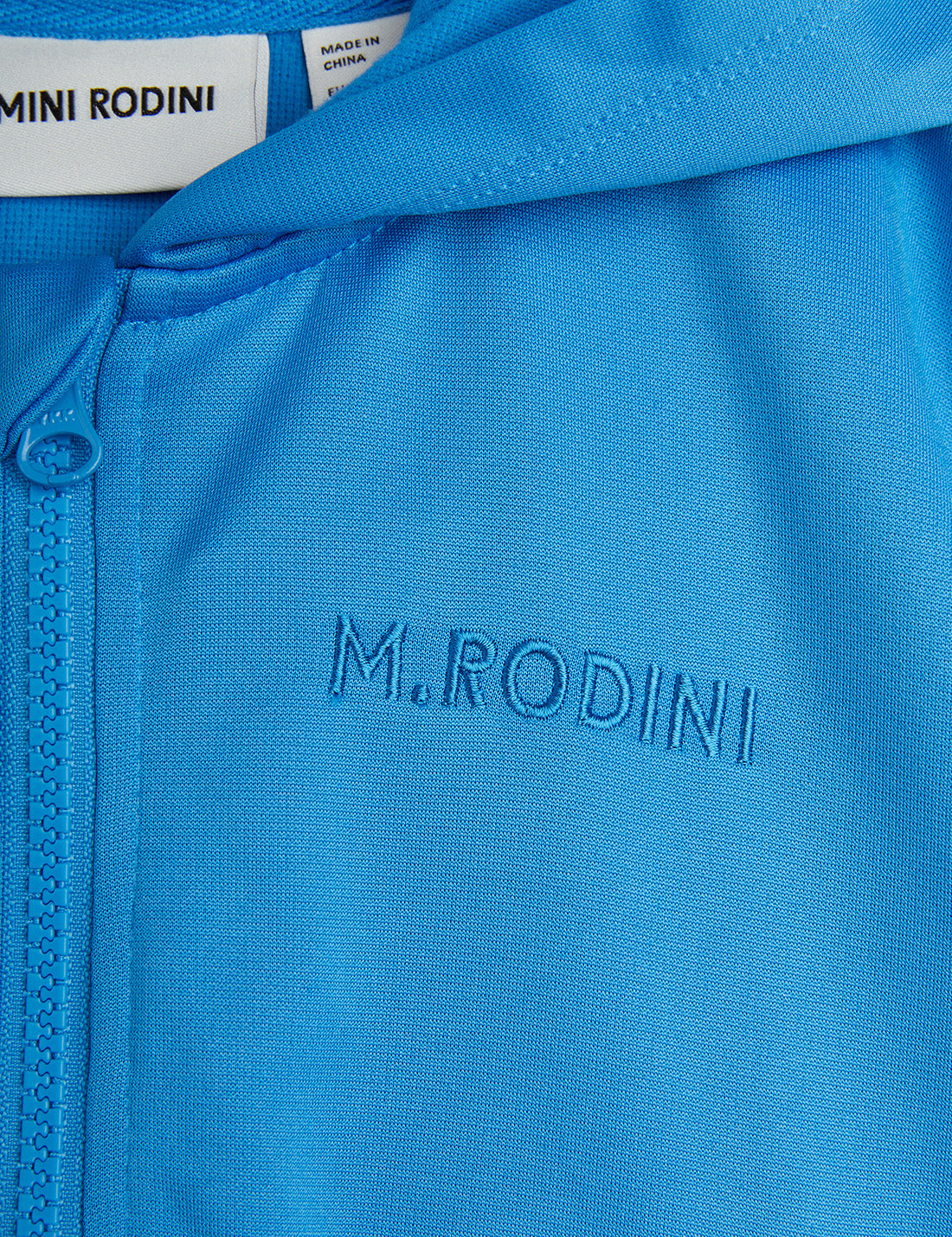 Close-up of the Mini Rodini WCT hoodie showing the tonal embroidered "M. Rodini" logo on the chest and matching blue zip with a branded zipper pull.