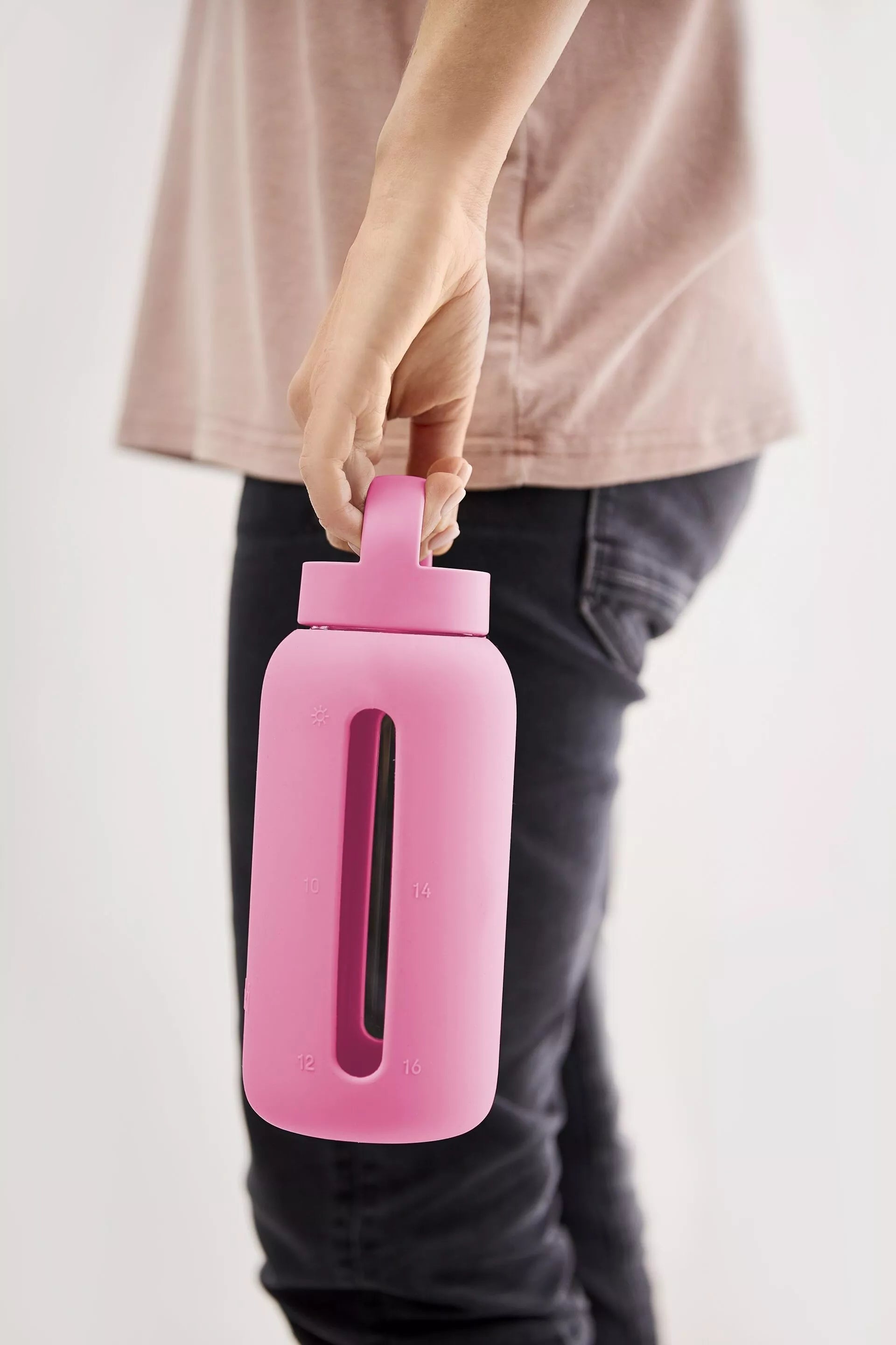 A matte Silicone covered glass bottle, with a window to see the drink on the inside, in a bright pink colour with a plastic screw top circular lid with a handle