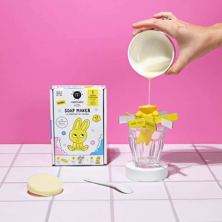 A hand pours liquid soap into the rabbit shaped mould of the Nailmatic kids soap maker The wall is bright pink and the tiles are white