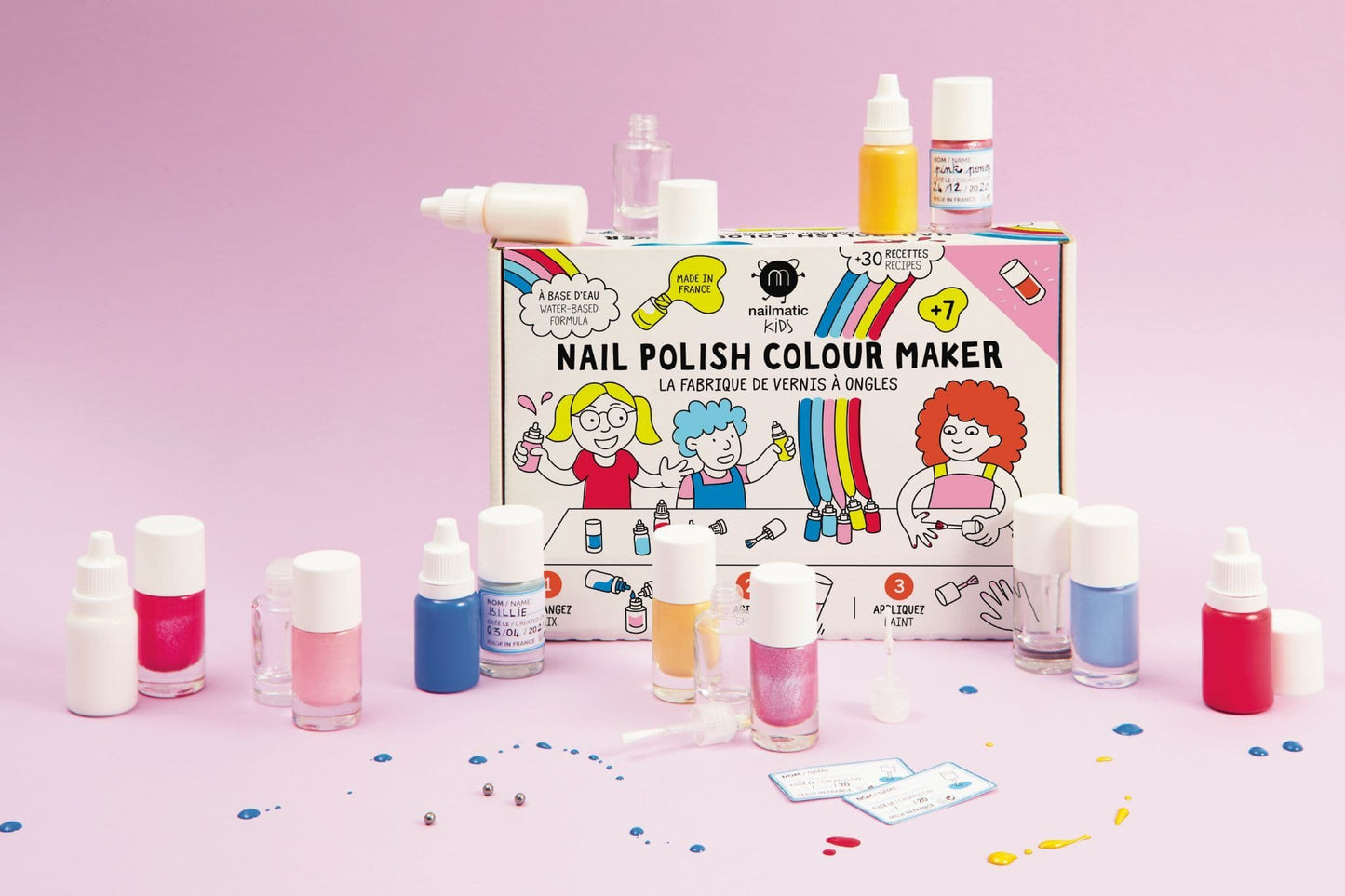 A Nailmatic Nail Polish Colour Maker kit showing 5 colourful and glittered solutions, 4 buildable bottles, a ruler, and labels for creating custom kids’ nail polishes.