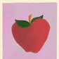 A Natalia Bagniewska Pomme print. The background is pink. It says “La Pomme” which means the apple in French. The apple is red in colour and then leaves are green. The stem is brown. Beneath the pink background, in black, on the left hand side it says An Apple A Day... and on the right it says ...Or So They Say