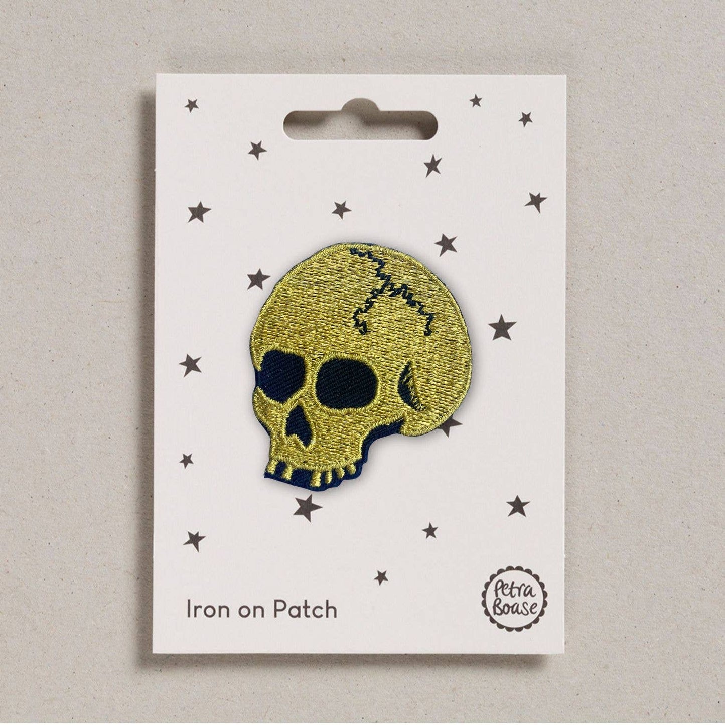 an embroidered golden skull. The skull has black eyes, nose and a black coloured crack on its head. The background is white with black stars  