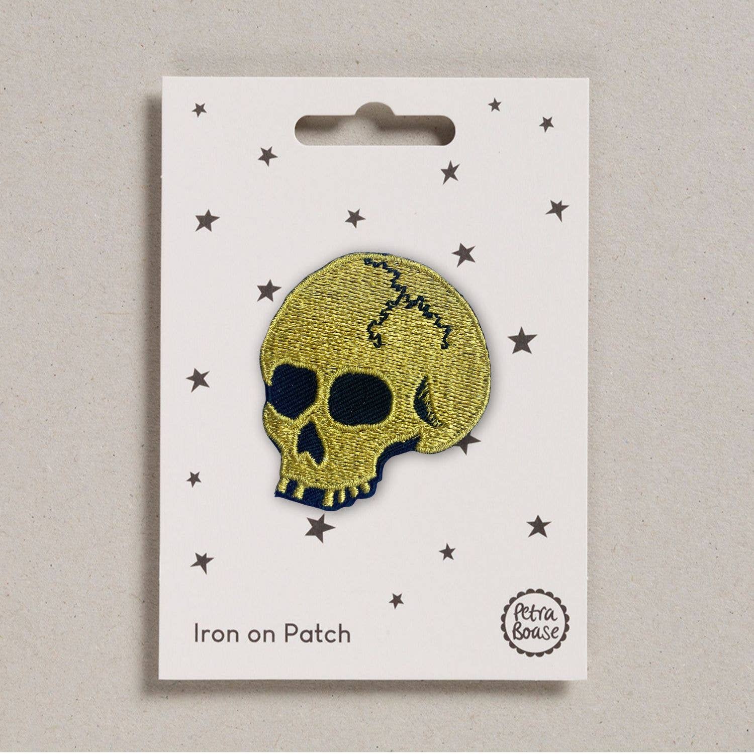 an embroidered golden skull. The skull has black eyes, nose and a black coloured crack on its head. The background is white with black stars  