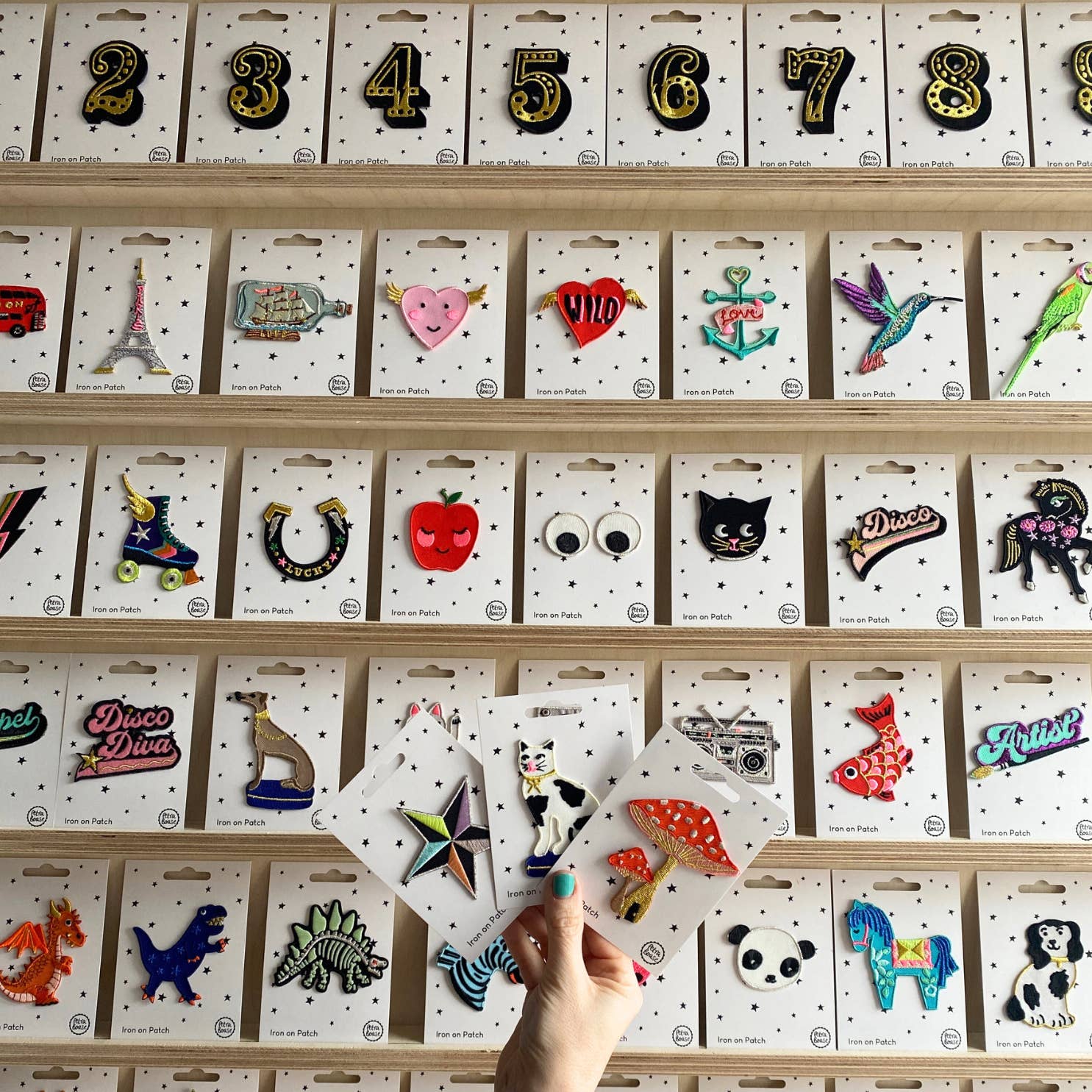 multiple multicoloured embroidered iron on patches. All of them have a white background with black stars. The woman is holding a cat, mushroom, starfish iron on patches. 