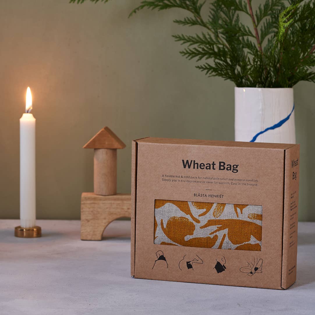 Wheat Bag packaging with a candle, wooden blocks, and plant in the background