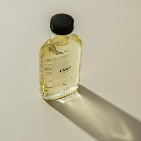 A glass bottle of luxurious body oil with a black lid and black writing, featuring translucent oil, elegantly positioned against a neutral background. The design highlights the nourishing blend of Ginger, Lemongrass, and Sweet Orange essential oils.