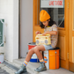 Person sitting on a stack of oil drums with a yellow boombox, wearing a yellow beanie and striped shirt, in front of a store entrance.