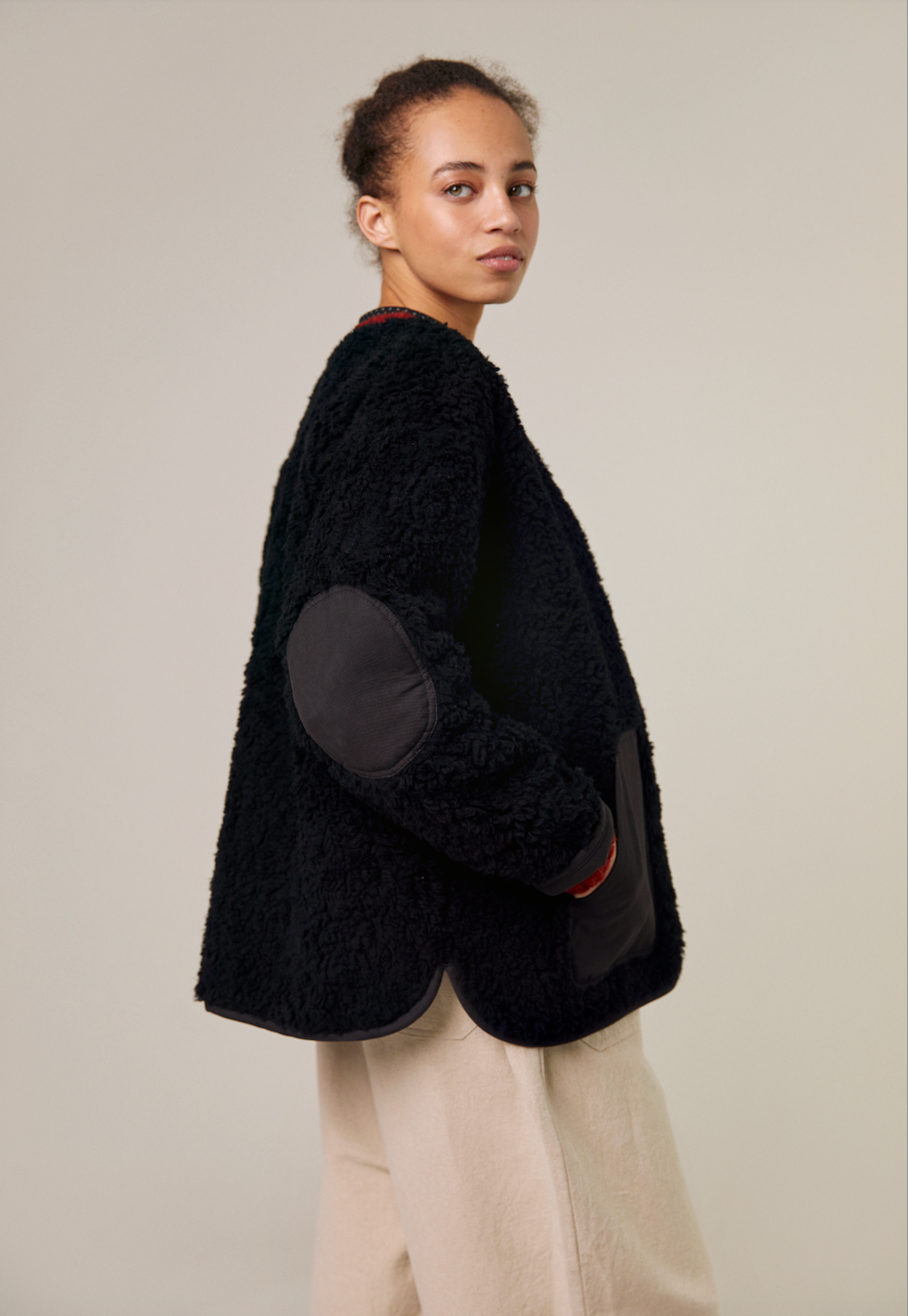 The Sideline Arc Jacket combines luxury and practicality, crafted from 100% wool shearling with a soft cotton lining. It features a zip-up front, elegant curved neckline, and contrasting elbow patches for added style. With a slightly oversized fit, this lightweight jacket offers warmth and comfort, making it a versatile winter essential.