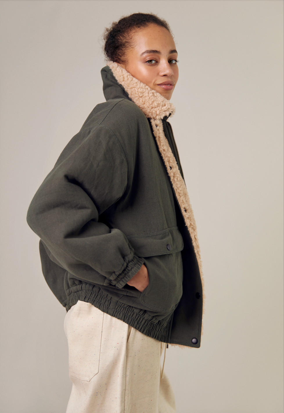 The Sideline Wilma Jacket displayed in reverse, highlighting the plush 100% shearling lining with a sleek olive cotton twill exterior. This view showcases the jacket's fully reversible design, featuring a zip front closure and rounded collar. The patch pockets are visible, emphasizing the stylish and functional aspects of this winter essential.