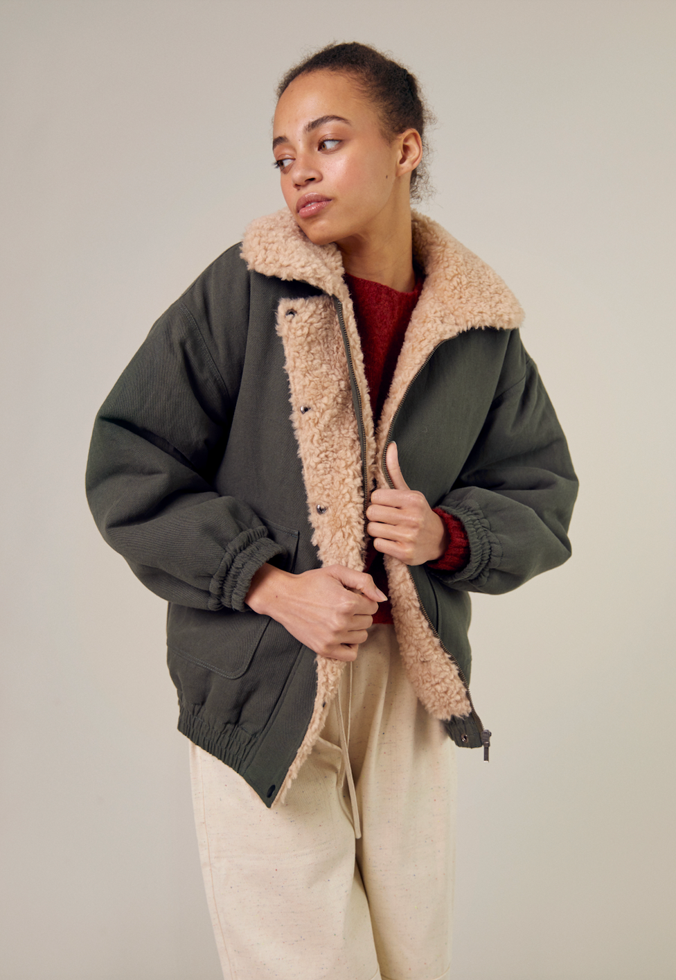 The Sideline Wilma Jacket, featuring the durable olive cotton twill side, worn by a model looking over her shoulder. The jacket showcases its stylish design with a zip front closure, snap-button placket, and rounded collar. The patch pockets are visible, highlighting the blend of practicality and elegance for winter wear.