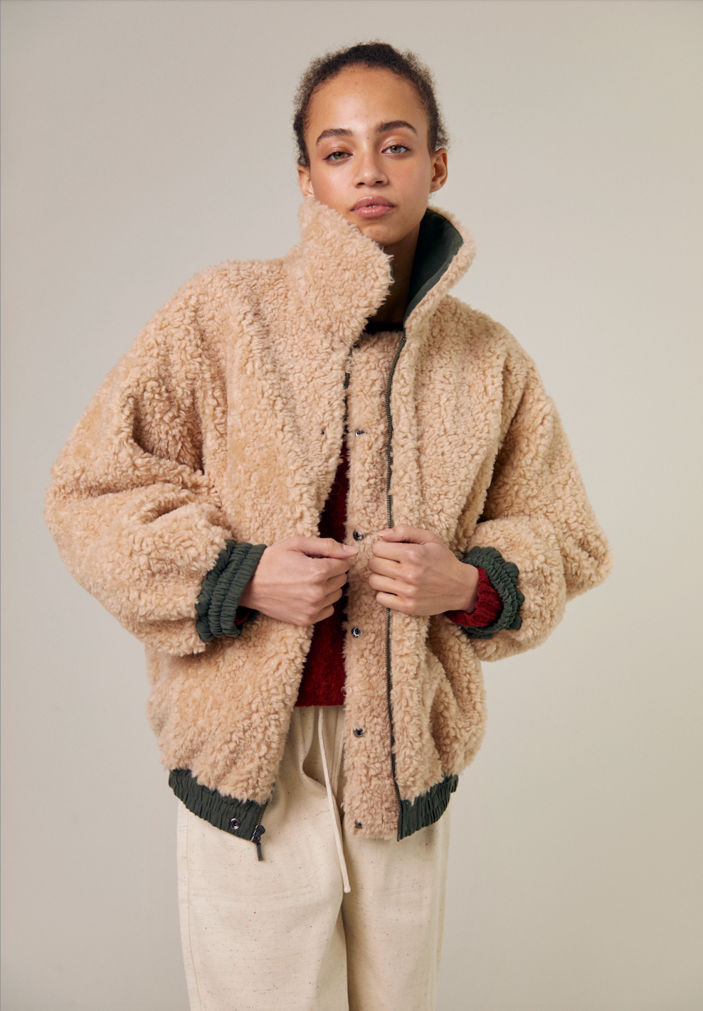 A close-up of a beautiful model wearing the Sideline Wilma Jacket with the plush shearling side facing outward. She holds the jacket together for warmth, highlighting its luxurious texture and cozy design. The soft shearling complements her look, emphasizing both style and comfort for winter wear.